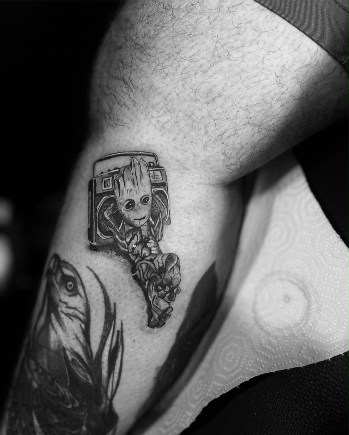Baby Groot with a boombox, black-and-grey micro-realism, lower leg — by Stefan Buttigieg